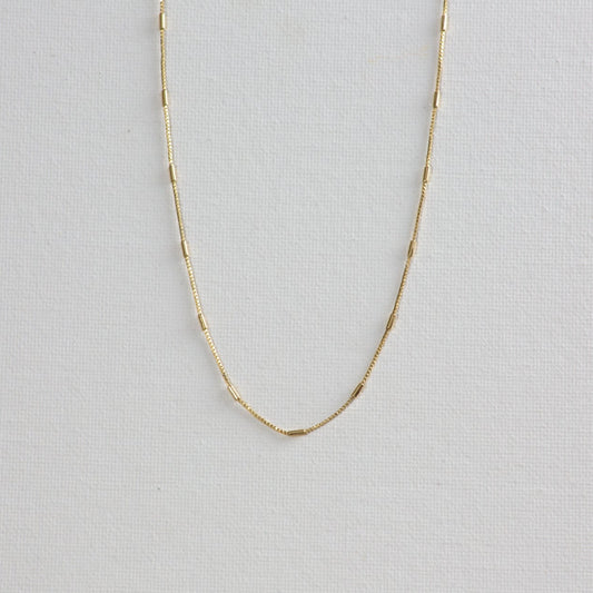 Morse necklace, a gold chain with alternating box chain and tiny gold bar, on a white background.