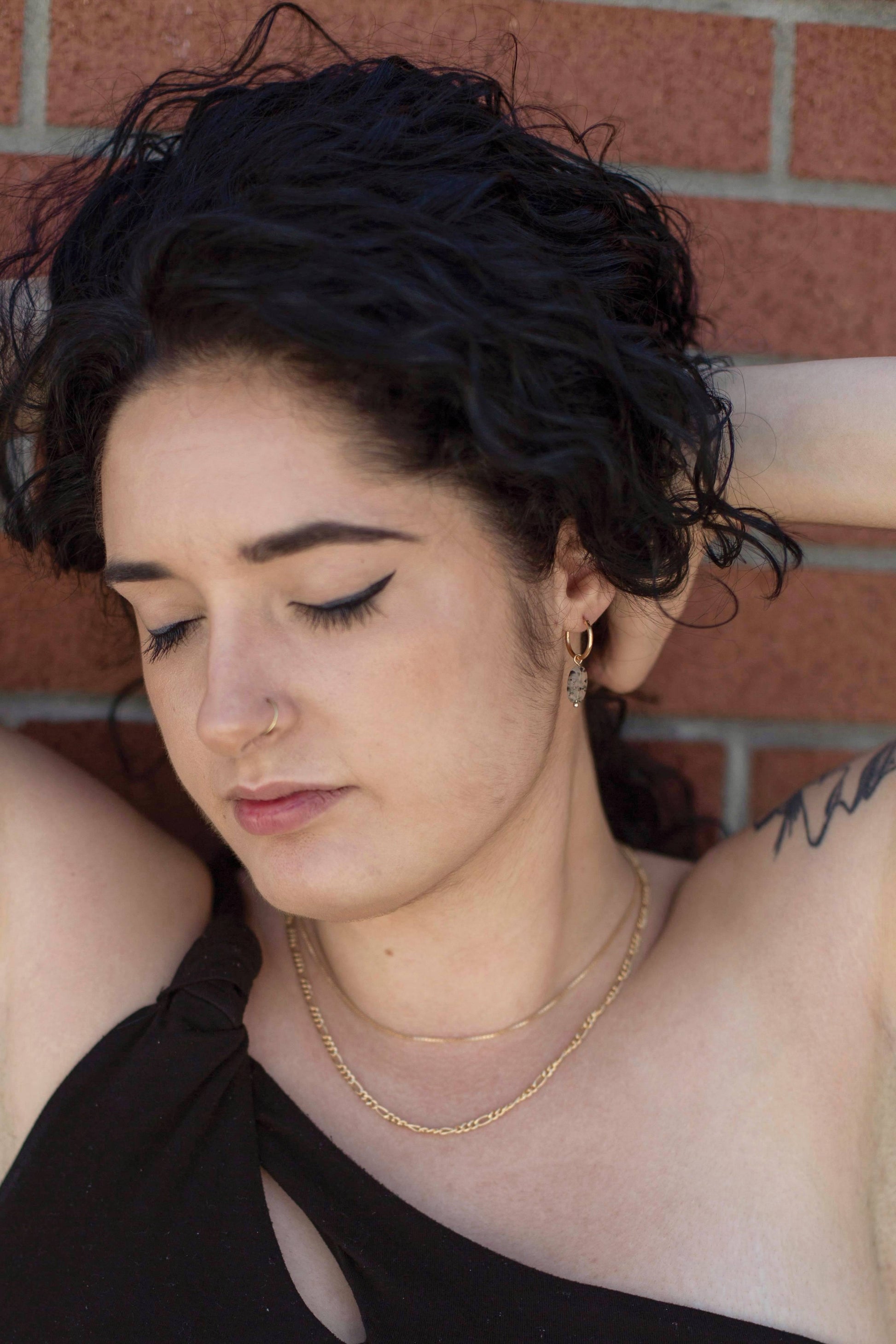  A model showcasing the hoop earrings with Dalmatian-like Black Rutilated Quartz Pendants, beautifully accentuating her look as she lifts her hair to reveal the accessory.